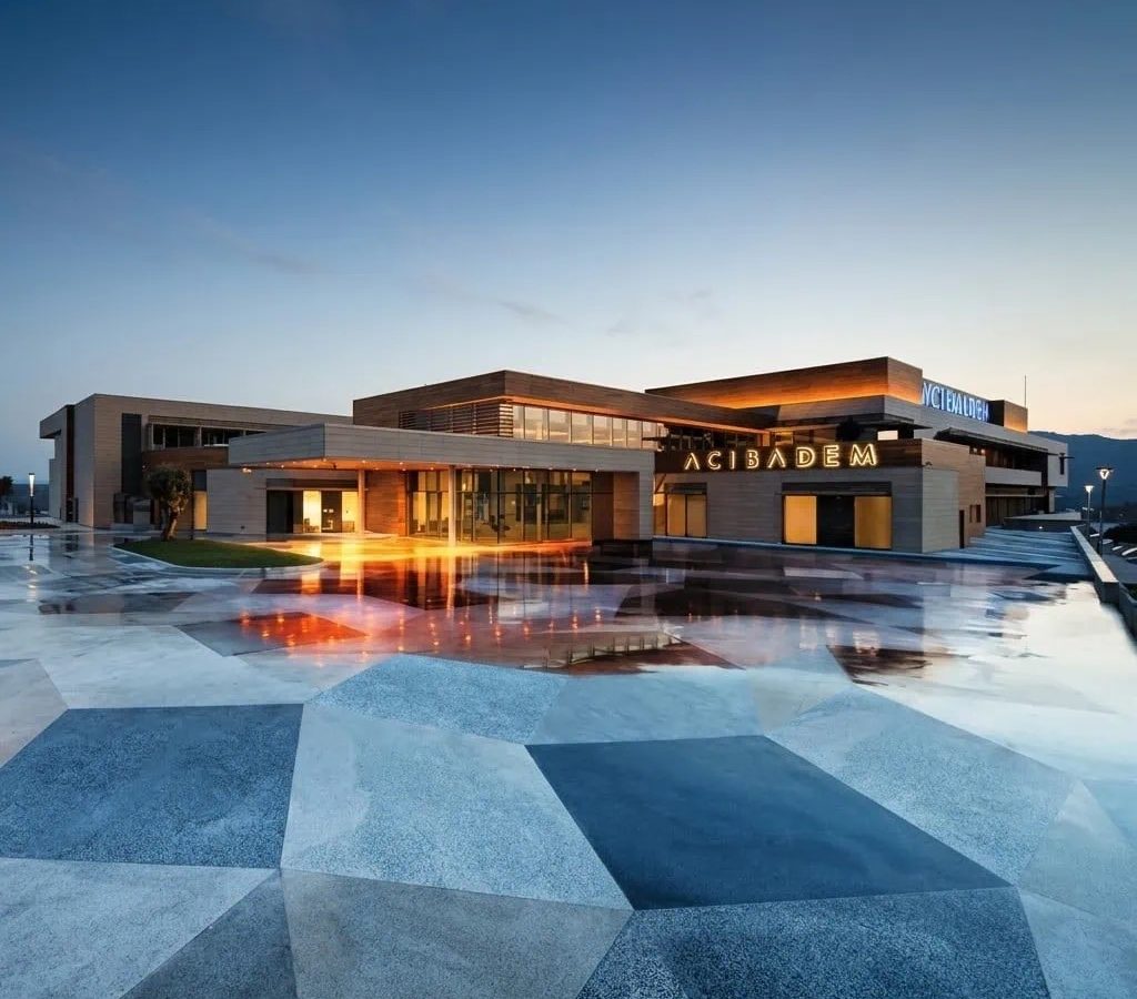 Modern exterior of Acibadem Bodrum Hospital at dusk with illuminated entrance.